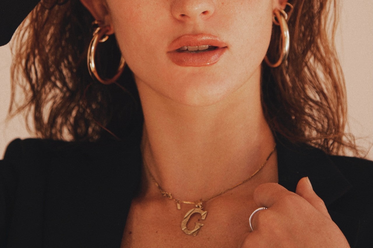 close up image of a woman wearing bold gold jewelry and a black blazer