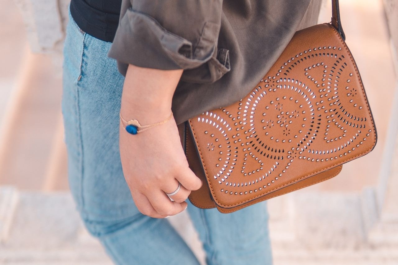 Married woman carrying a leather purse shows off a minimalistic sapphire gold bracelet paired with an accenting bracelet