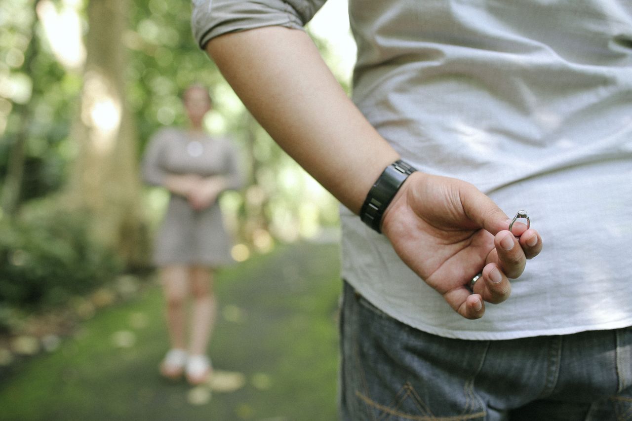 A man holds a bezel set engagement ring behind his back moments before proposing