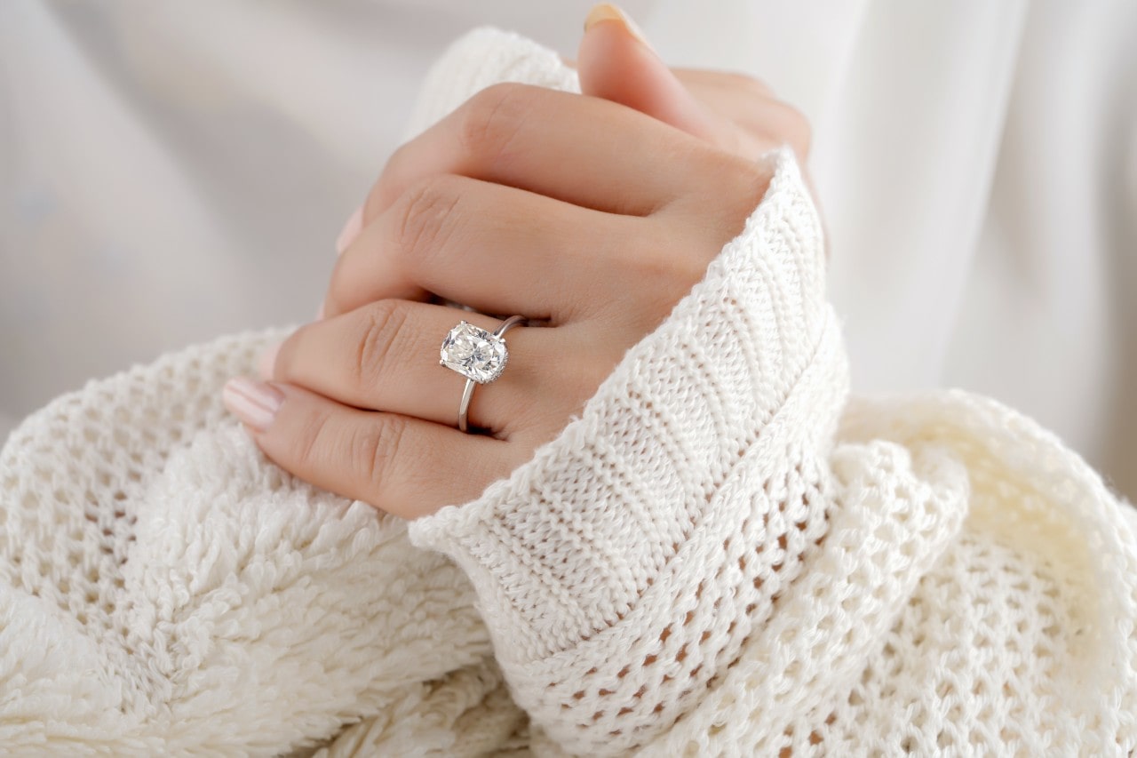 Woman’s hand wearing a radiant cut diamond engagement ring and a white sweater