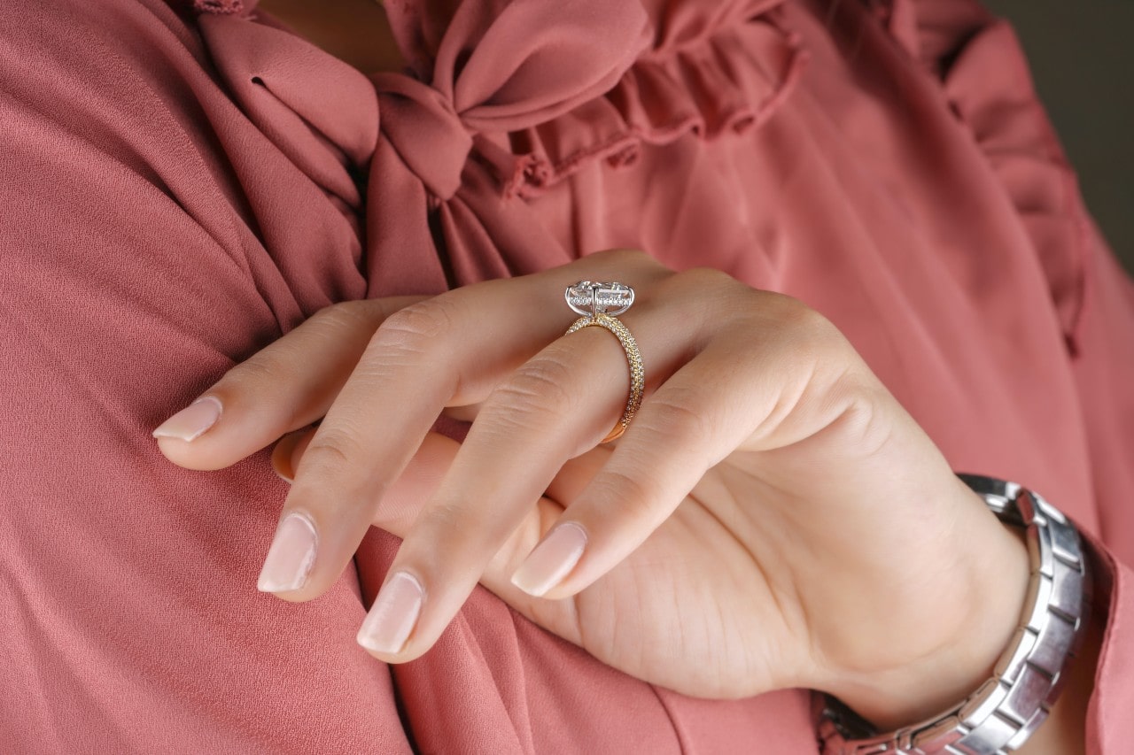 A woman wearing a pink shirt, a silver watch, and a gold engagement ring