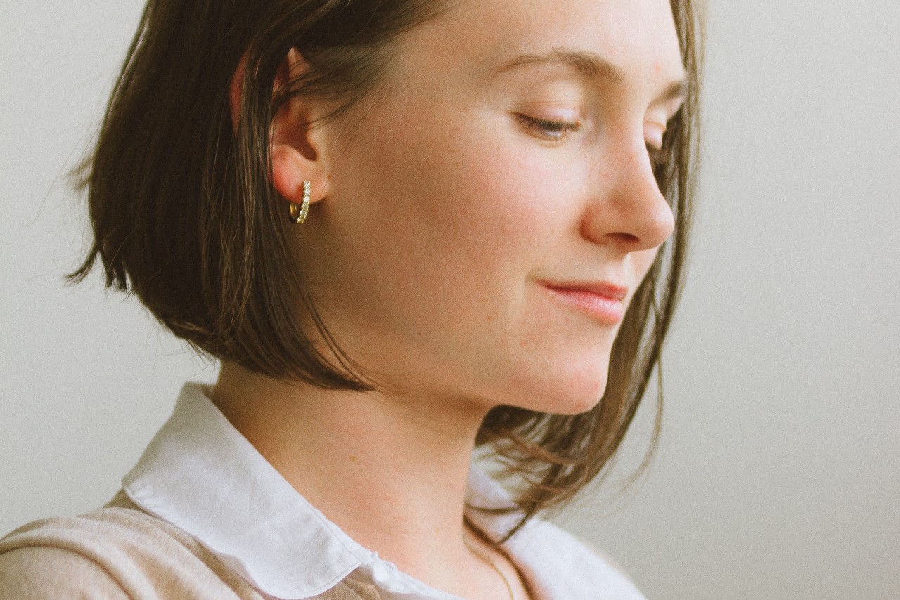 a woman wearing a pair of small gold huggies earrings.