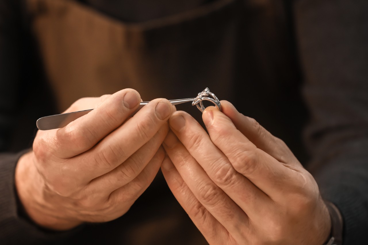 A close up of a jeweler’s hand inspecting with tweezers silver engagement ring