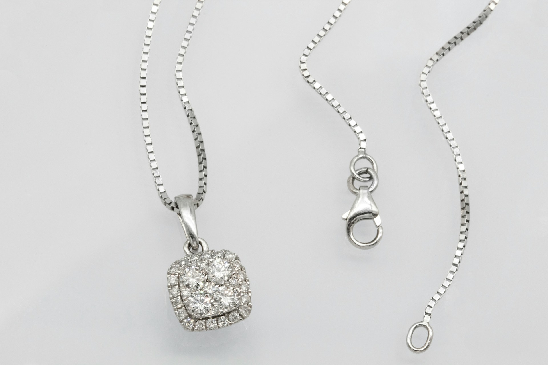 a white gold diamond pendant necklace on a plain gray surface