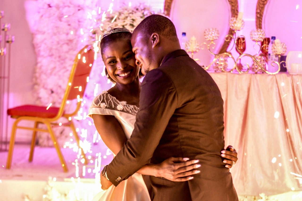 A joyful couple dances closely at their wedding, surrounded by sparkling lights against a beautiful flower background.