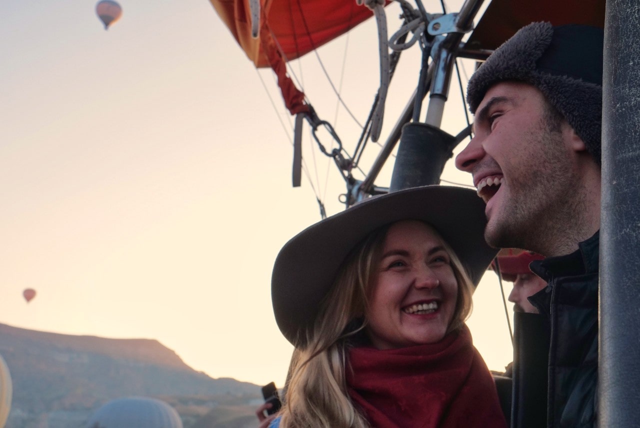 A joyful couple in a hot air balloon basket at sunrise, laughing and smiling.