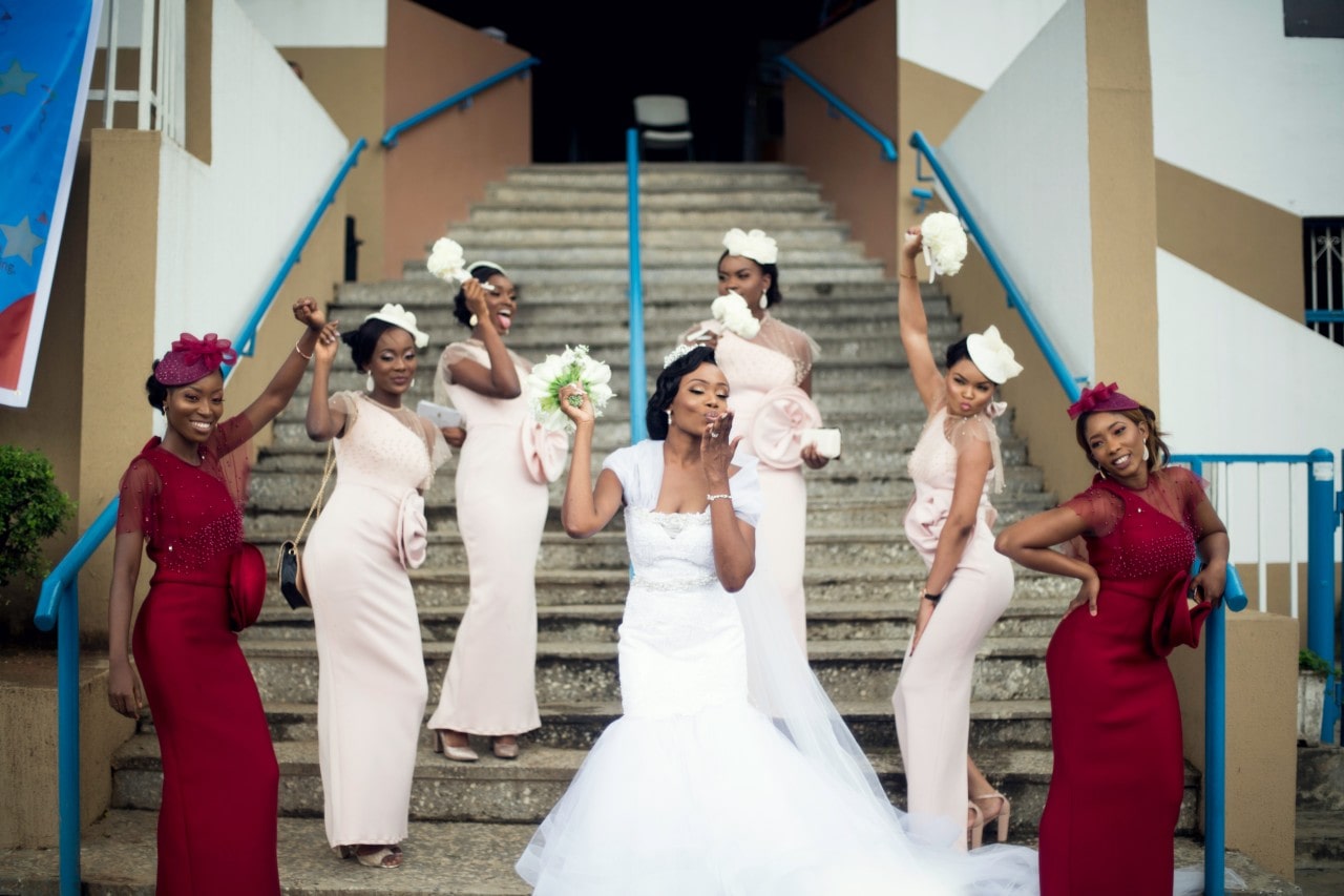 Bride, maids of honor, and bride&rsquo;s maids outside of a local building, posing on their steps