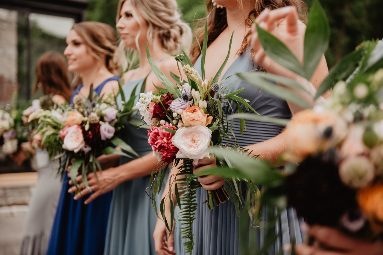 Several bridesmaids in grey and deep blue dresses hold bouquets and stand in the line.