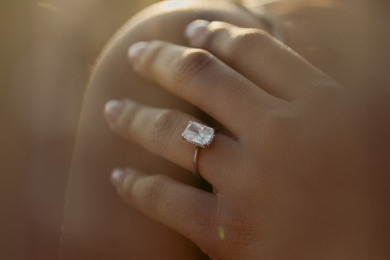 A closeup of a woman’s hand wearing a radiant engagement ring on a hazy day.