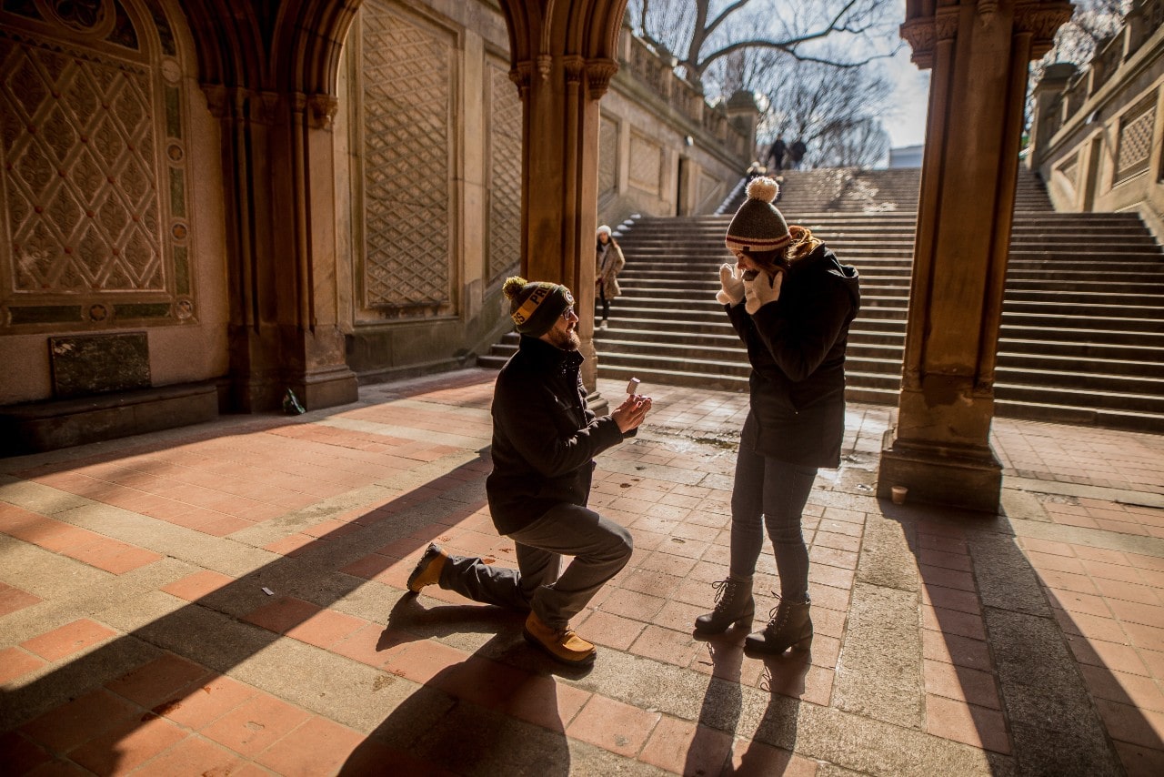 A man proposes to his surprised girlfriend in a historical plaza.
