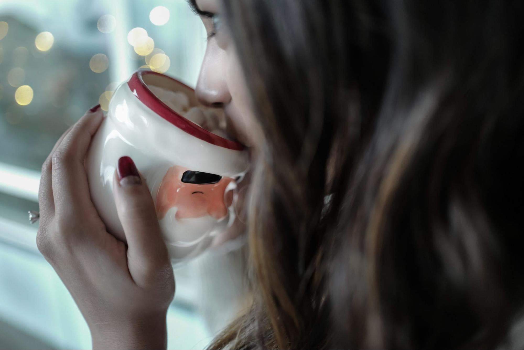 A fiancee sips hot cocoa out of a Santa-themed mug on a snowy night.