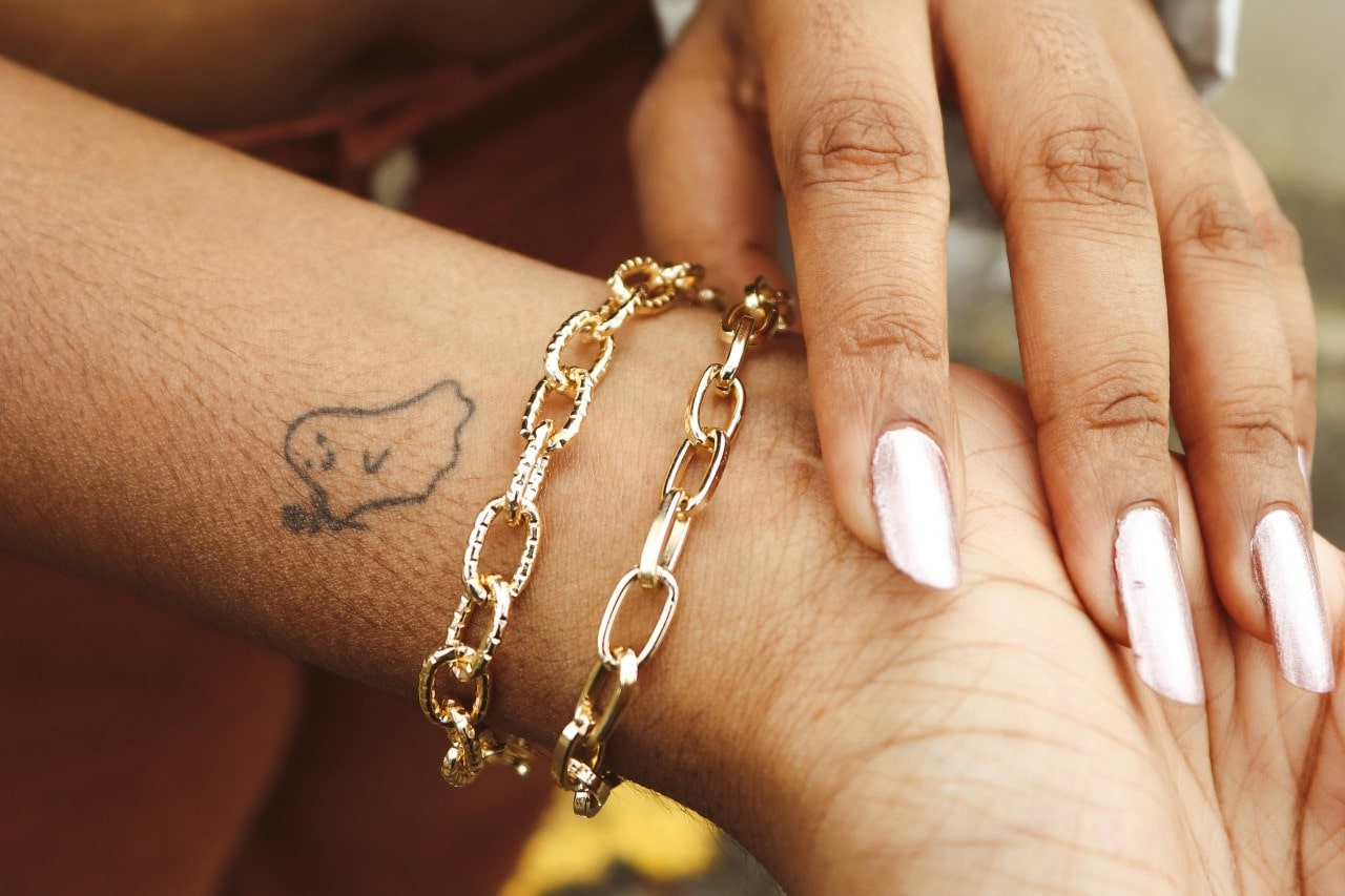 close up image of a woman’s wrist wearing two chunky gold chain bracelets