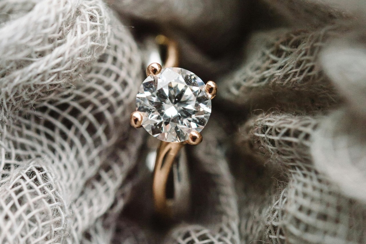 A rose gold solitaire round diamond engagement ring nestled in a decorative crochet item.