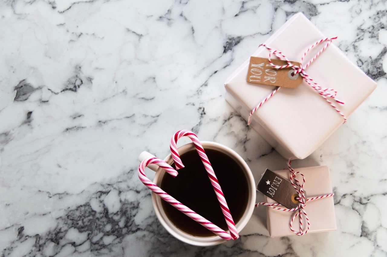A coffee cup with two candy canes and two gifts on a marble countertop.