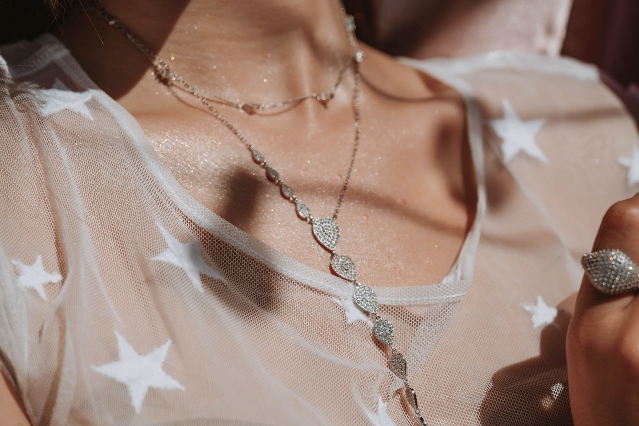 a woman in a star printed shirt wearing a long diamond necklace and a diamond ring