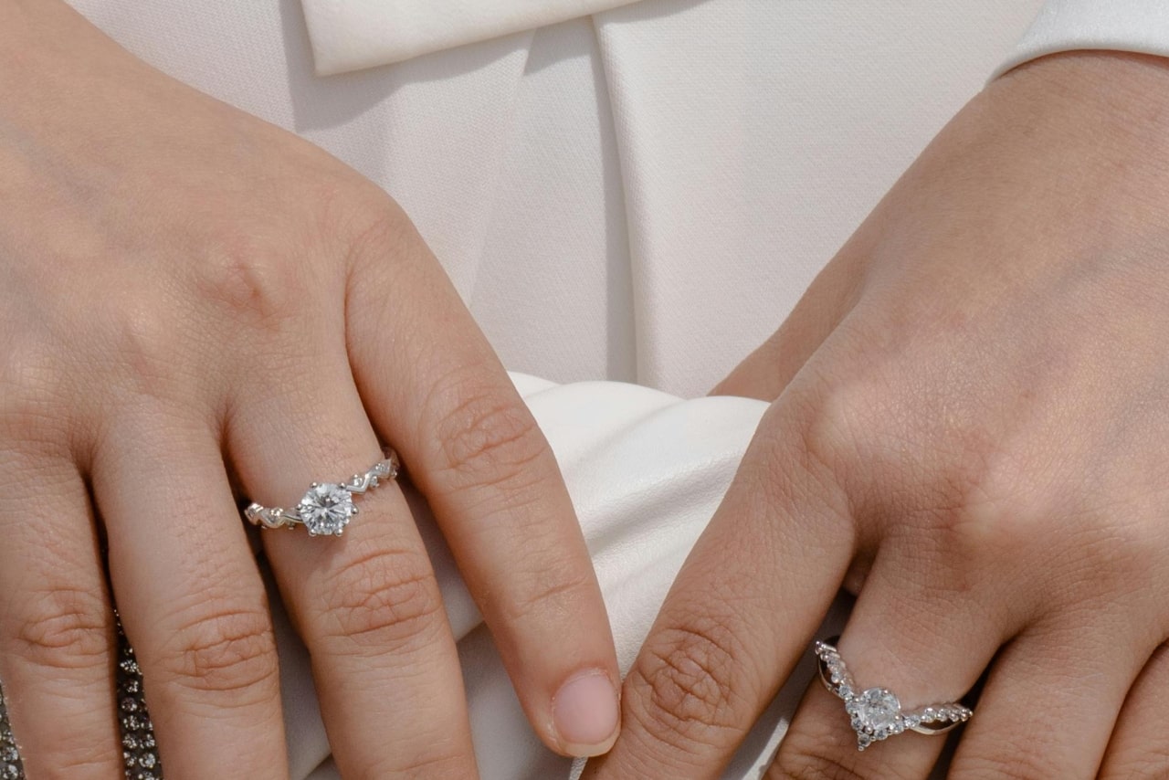 A close-up of a woman’s hands adorned with elegant diamond rings, both featuring intricate band designs.