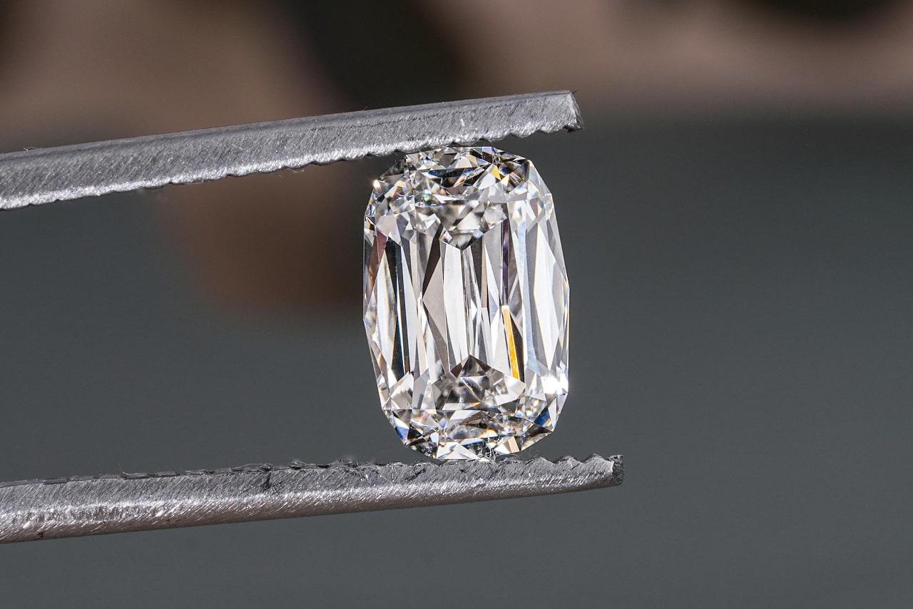 A close-up of a radiant cut diamond held by jeweler’s tweezers.