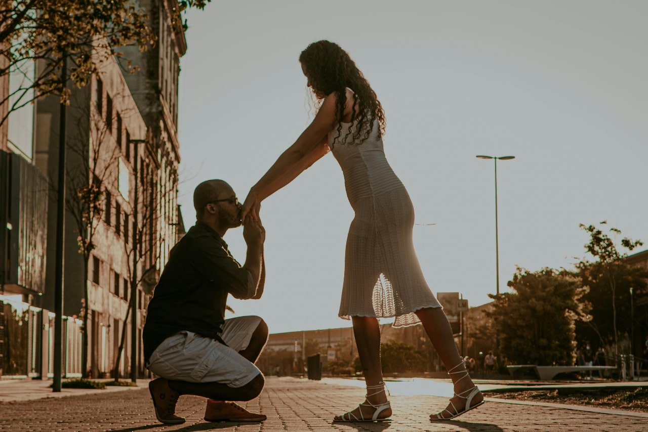 Man kissing a woman’s hand after he proposed on a sundrenched city street.