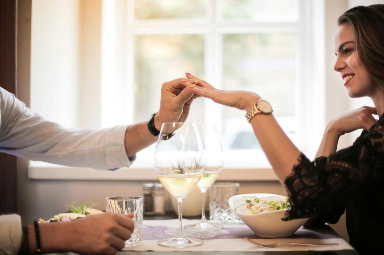 A man slipping an engagement ring on his partner’s finger over dinner.