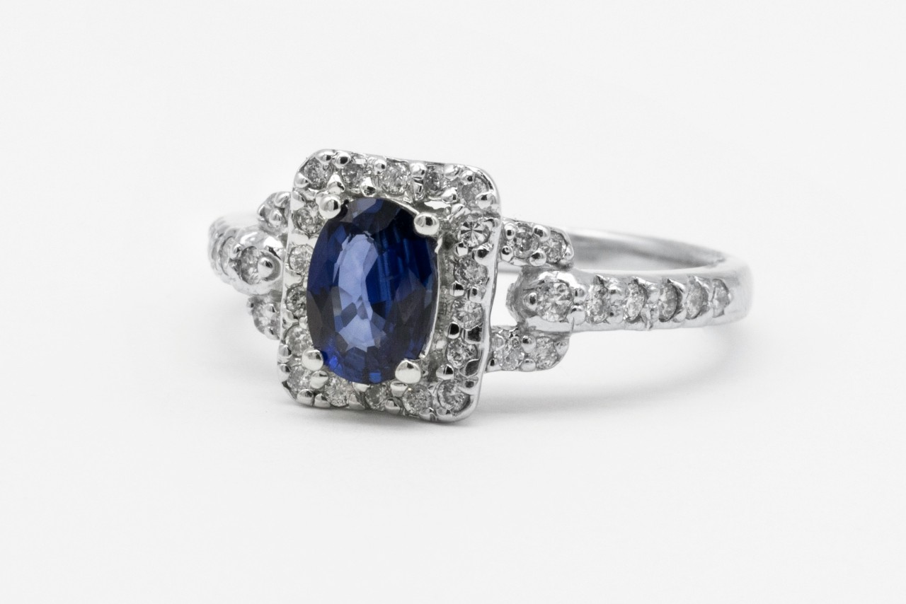An elegant white gold engagement ring with an oval cut sapphire center stone in a square halo setting.