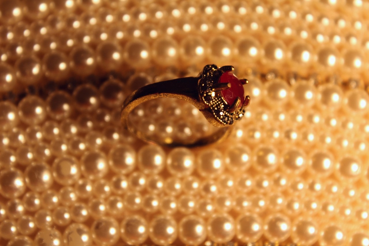 A silver halo ring with garnet round center stone against a pearl background