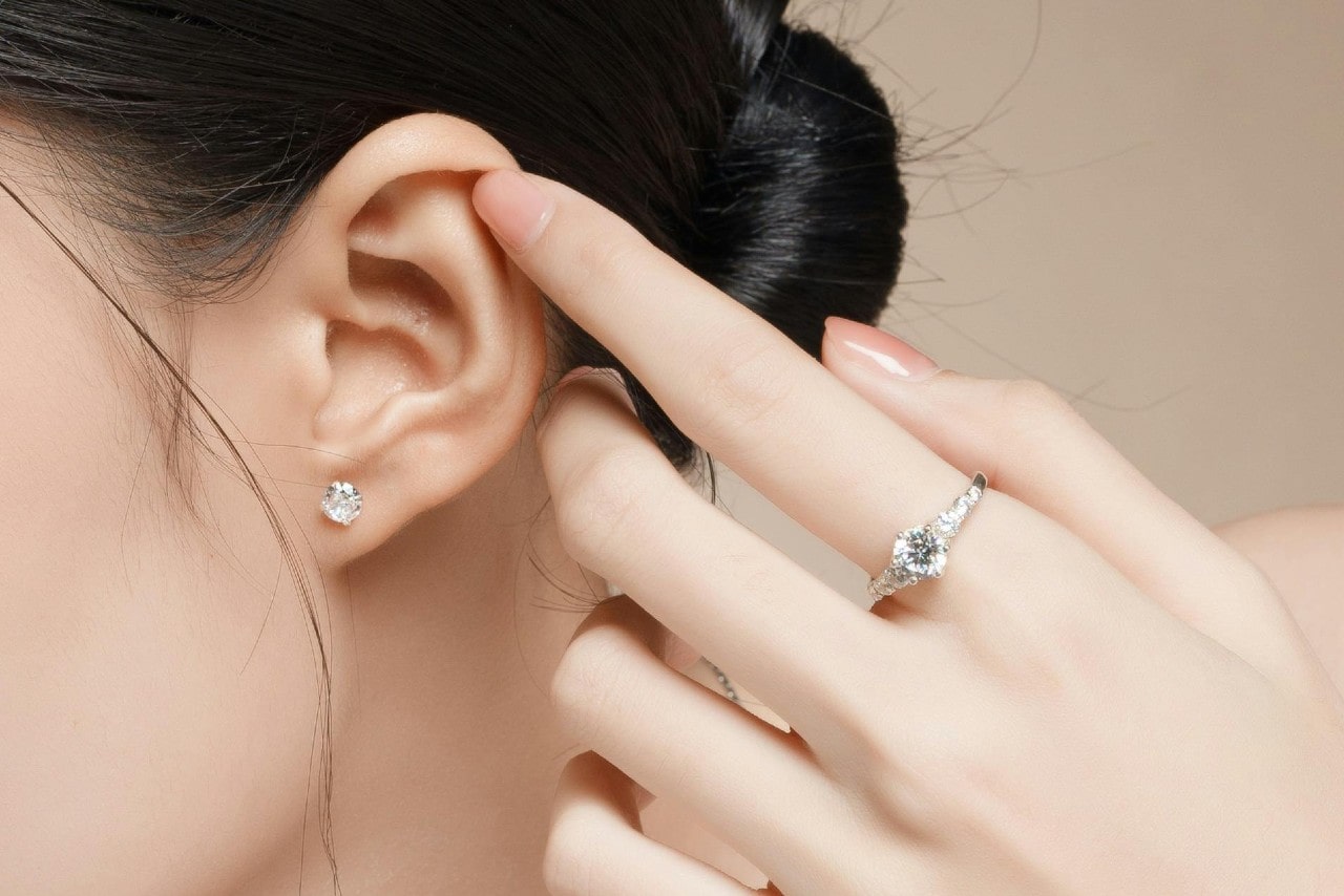Close-up of a woman's ear with a sparkling stud earring and a hand beside it wearing a diamond ring.