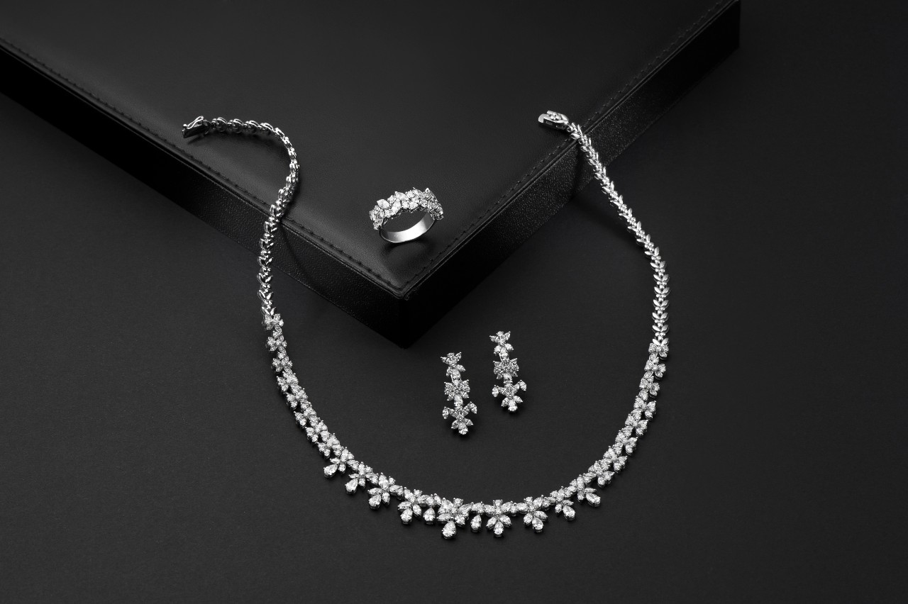 A matching diamond necklace, drop earrings, and fashion ring on a black surface.