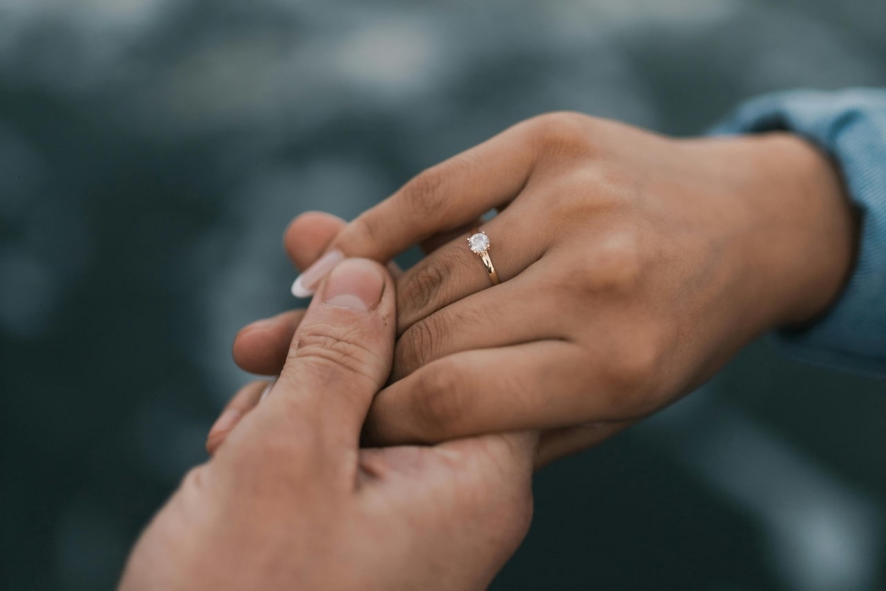 A yellow gold solitaire ring on the hand of a woman holding her partner’s hand