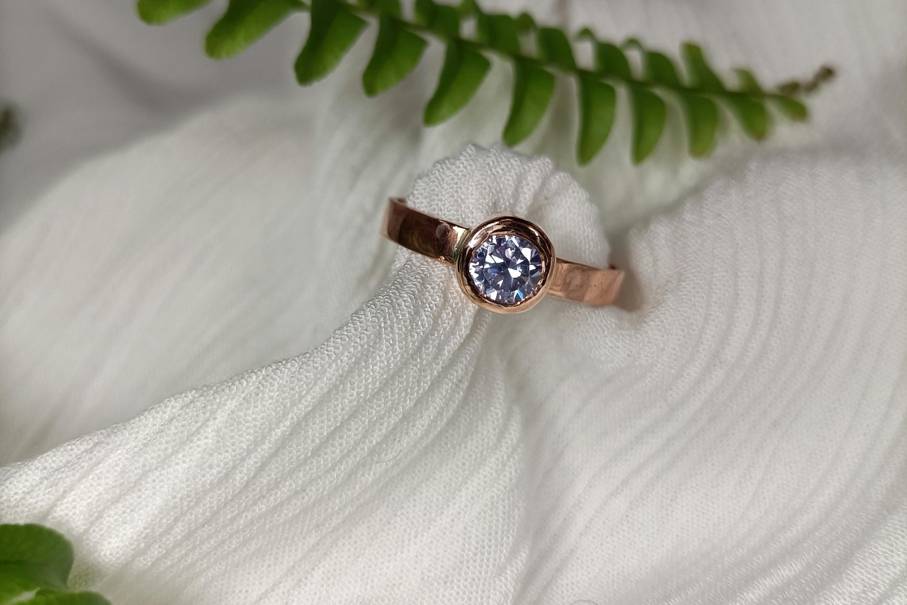 A rose gold band with a bezel set brilliant round diamond