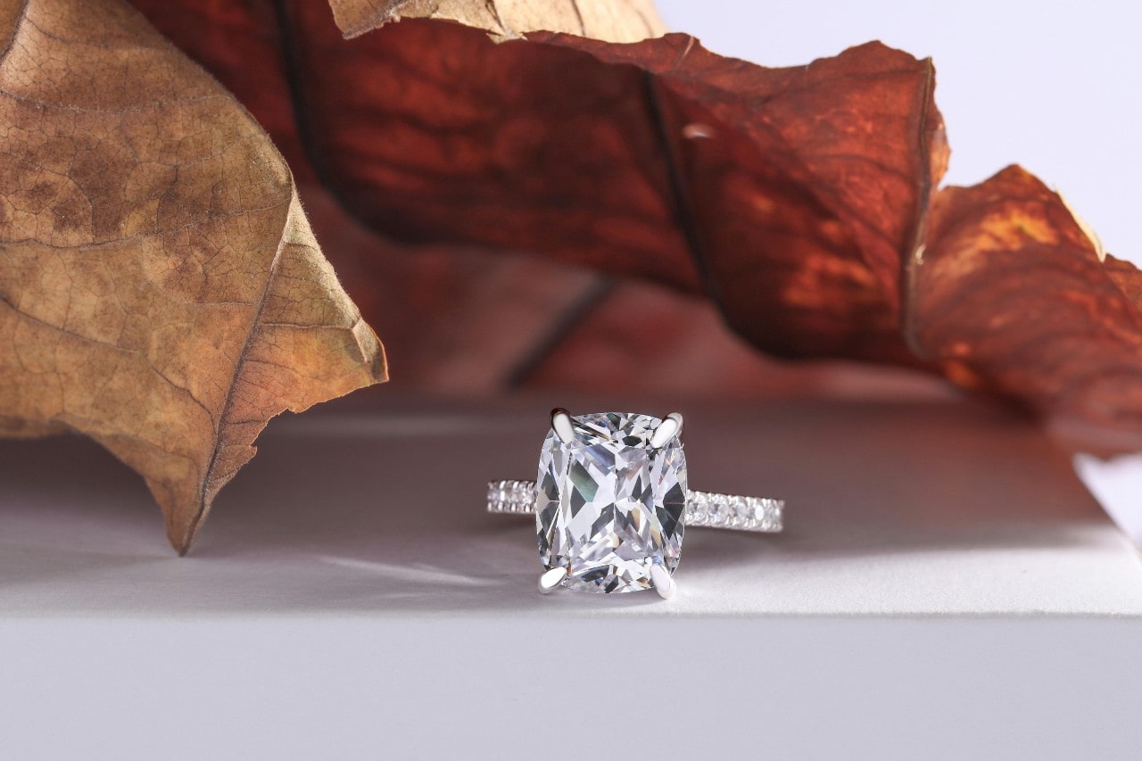 a white gold engagement ring featuring a large diamond center stone, under a leaf