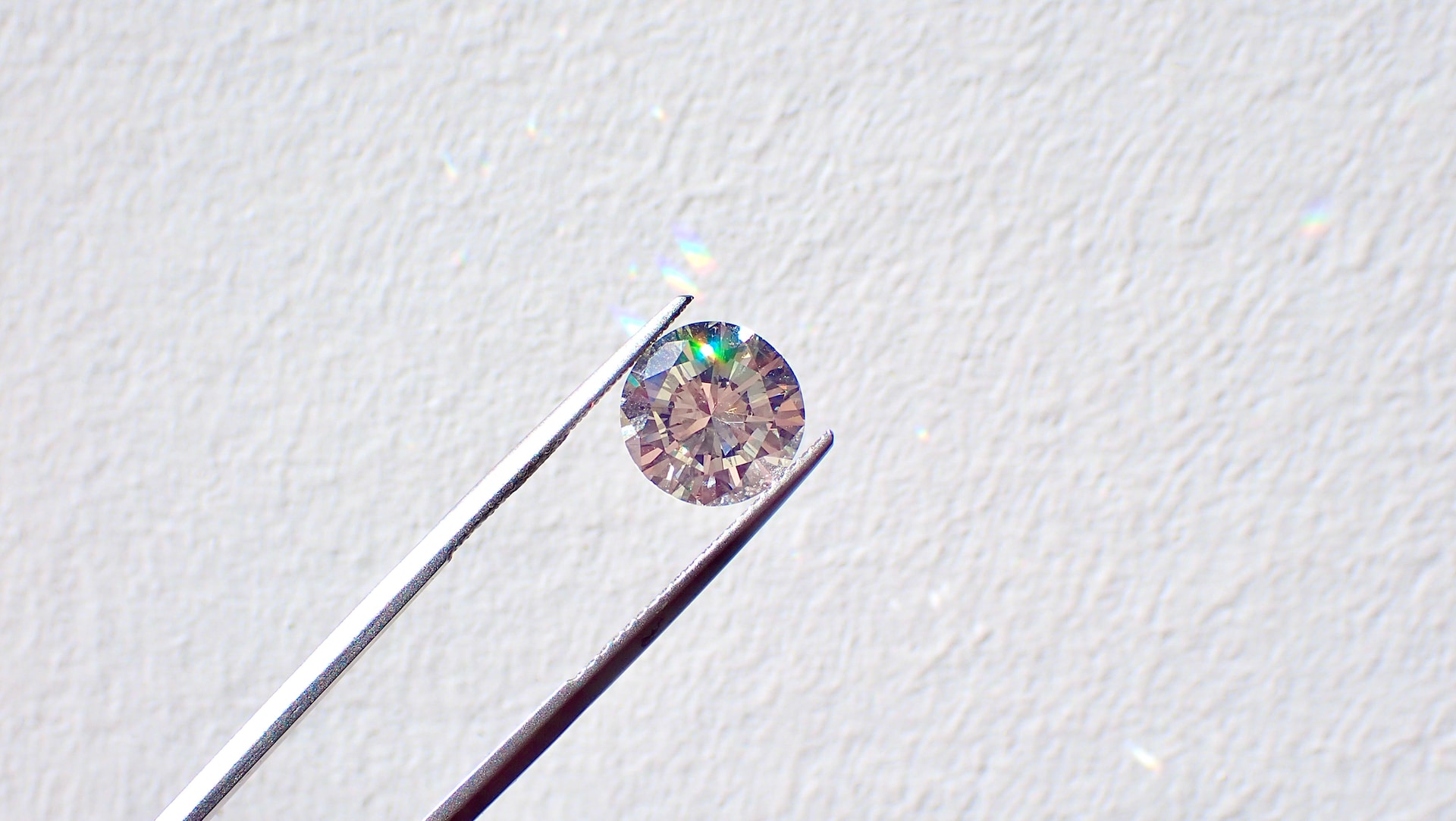 a round cut diamond being held in a pair of tweezers against a white background