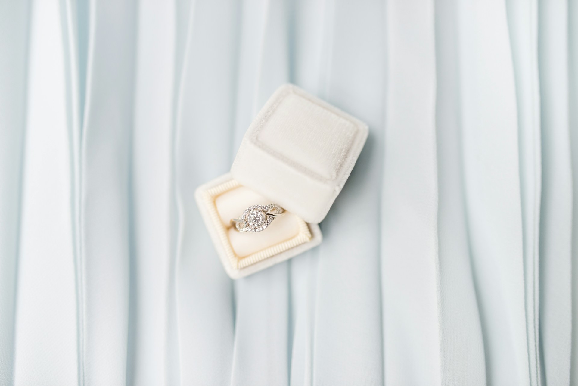 a diamond engagement ring in a white jewelry box on a light blue background