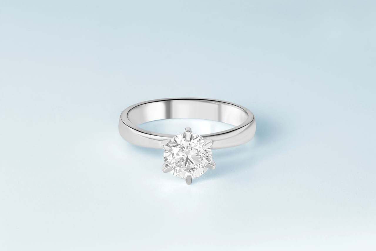 A close-up of a sleek and pristine solitaire engagement ring on a pale blue backdrop.