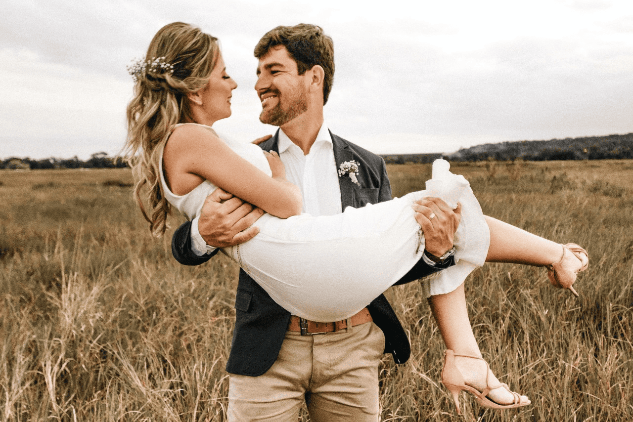 a groom lifts his bride while standing in a field as the sun sets.