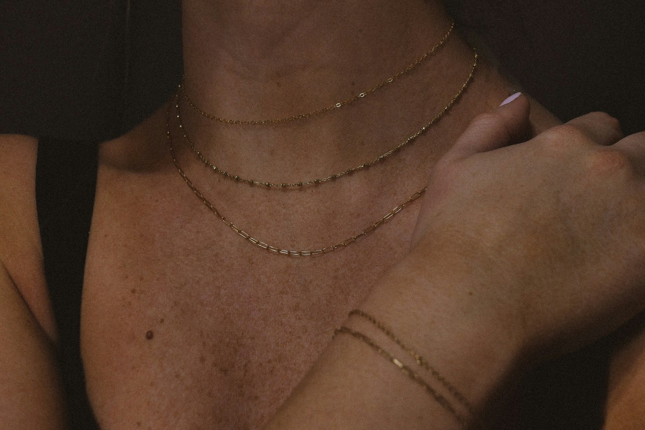 a woman’s neckline adorned with three small chain necklaces
