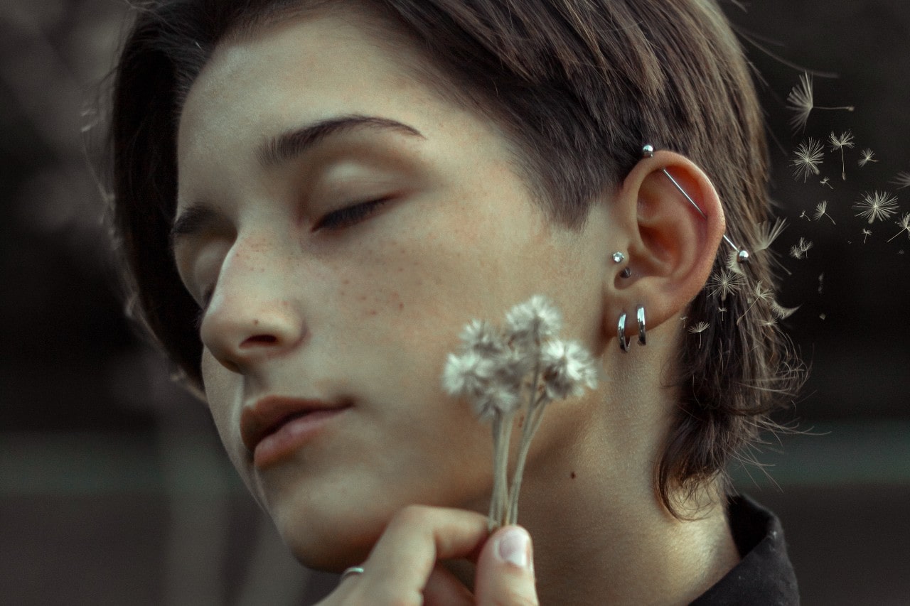 a woman holding flowers up to her cheek and wearing four different earrings