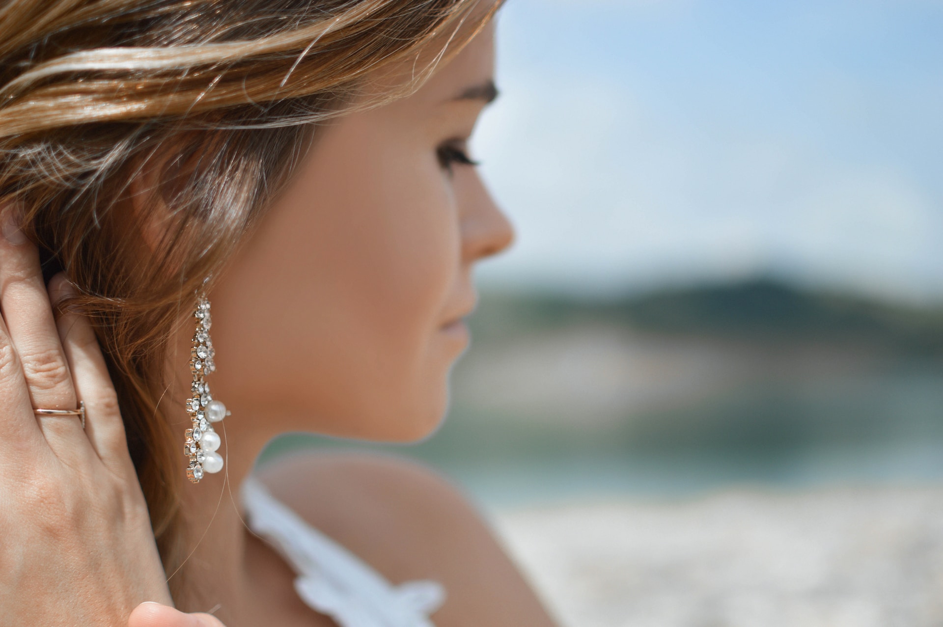 a lady wearing diamond and pearl earrings on a beach