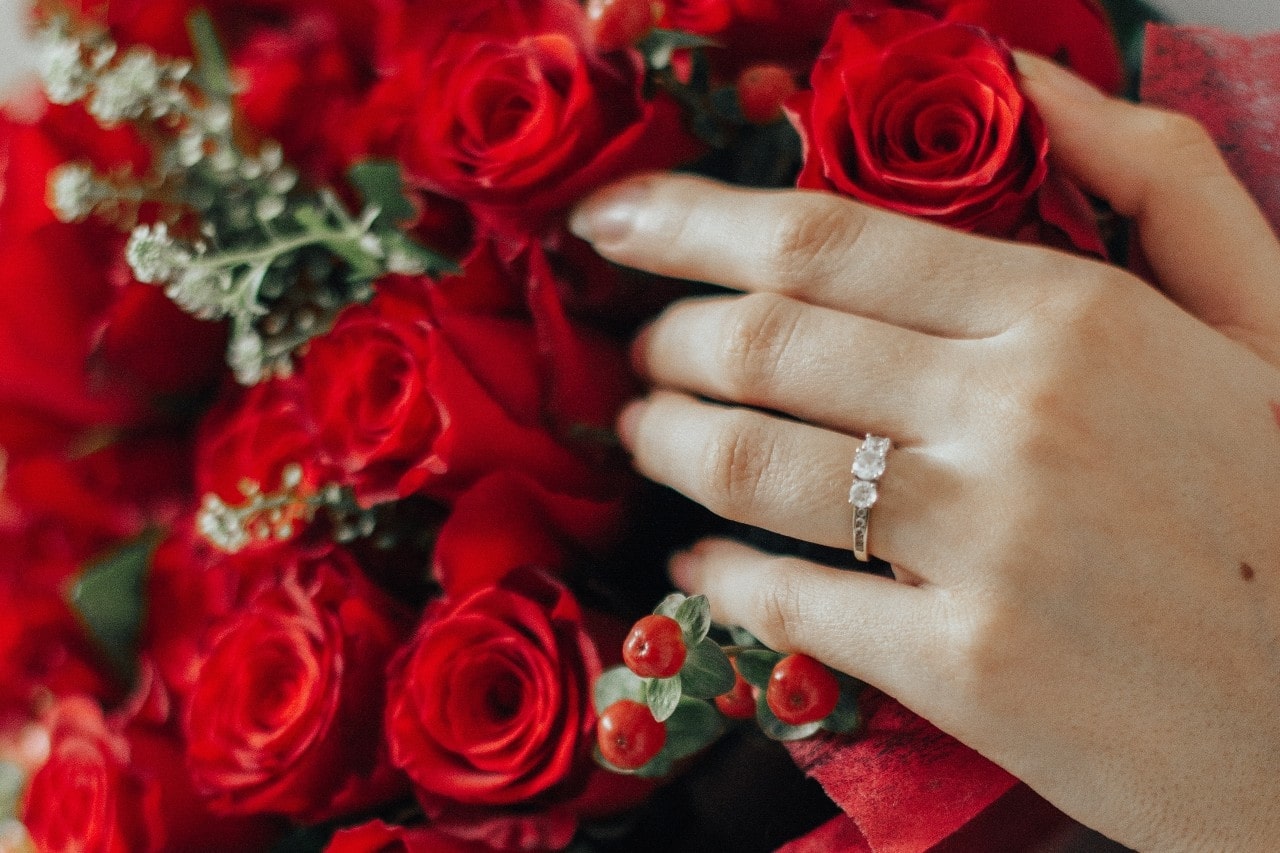 a hand wearing a diamond ring and a bouquet of roses