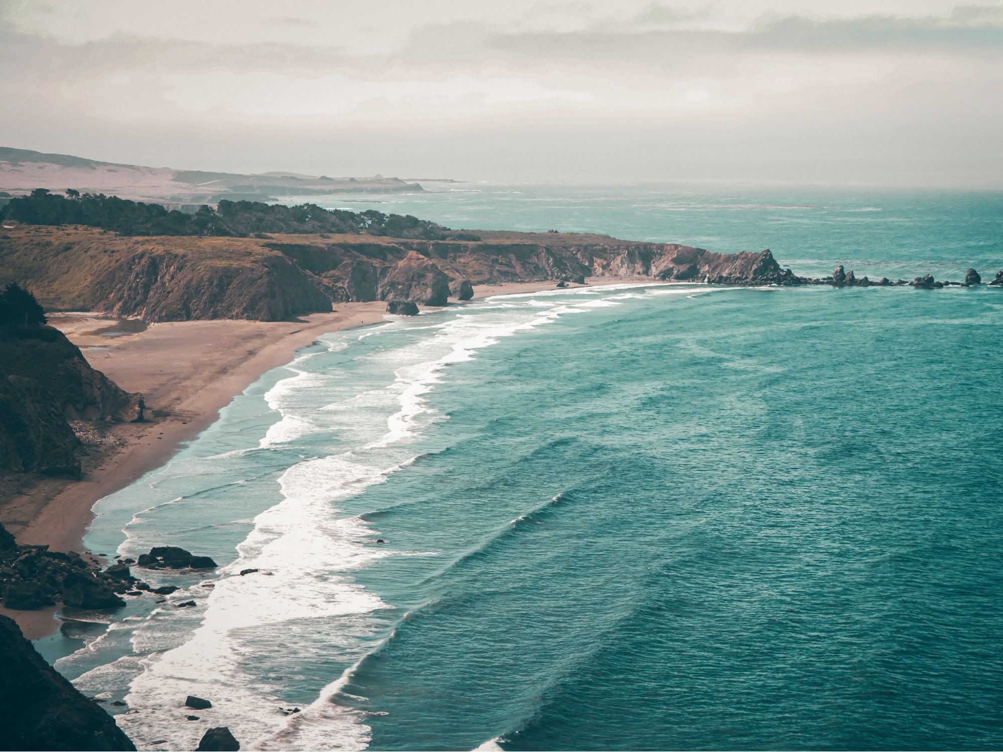 a distance shot of a rugged oceanic coastline with rocks and waves