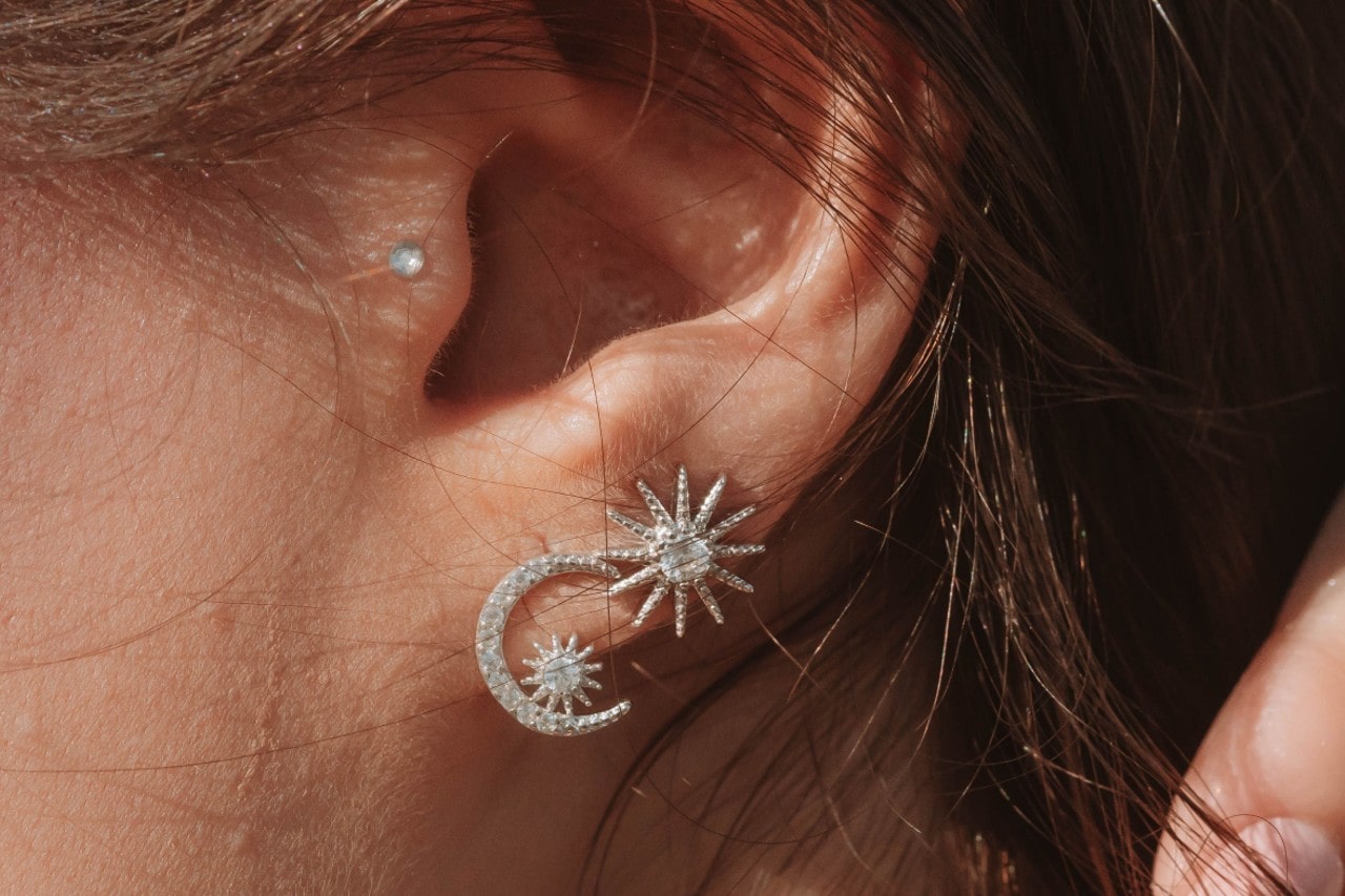 close up image of a person’s ear wearing sun and moon diamond earrings