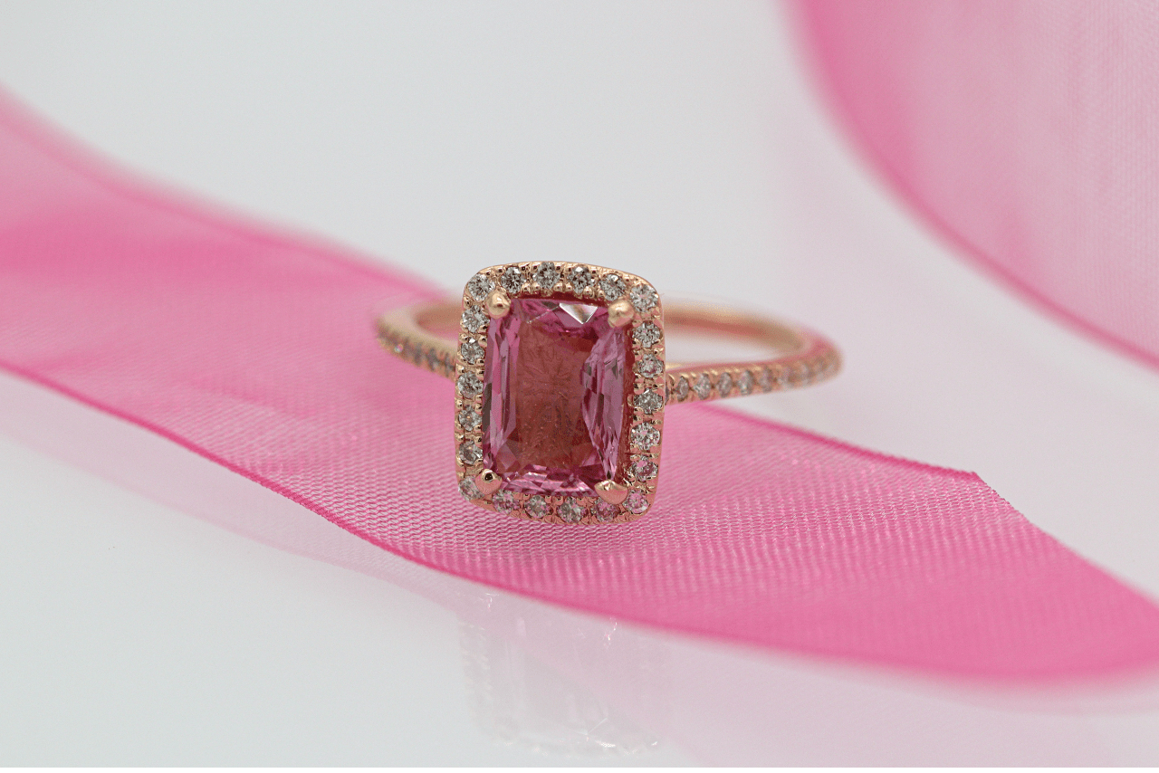 A rose gold engagement ring with pink gemstone on top of the pink ribbon.