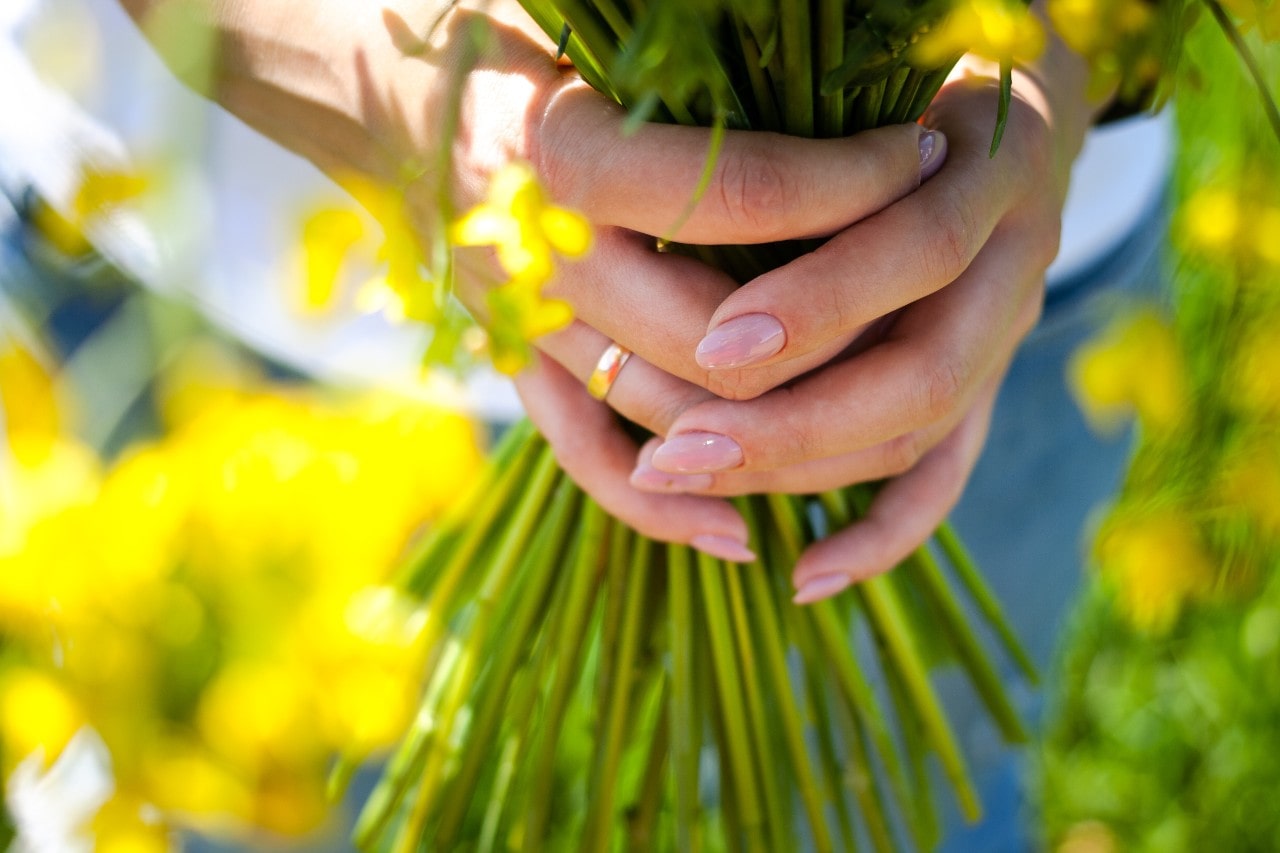 A close-up of a woman’s hands adorned with a simple gold band, holding a bouquet of flowers.