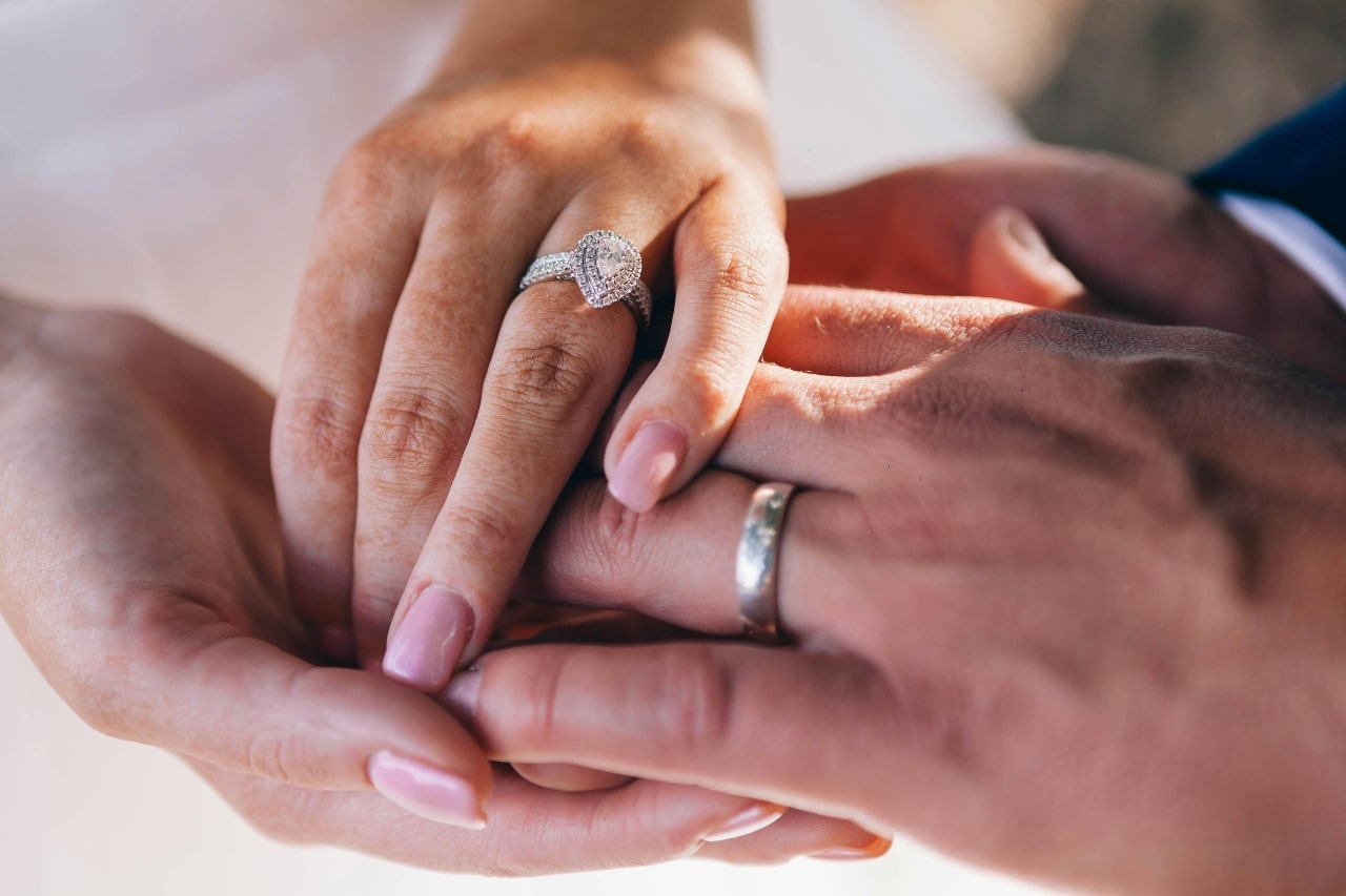 A close-up of a newlywed couple holding hands, with emphasis on the bride’s opulent engagement ring.