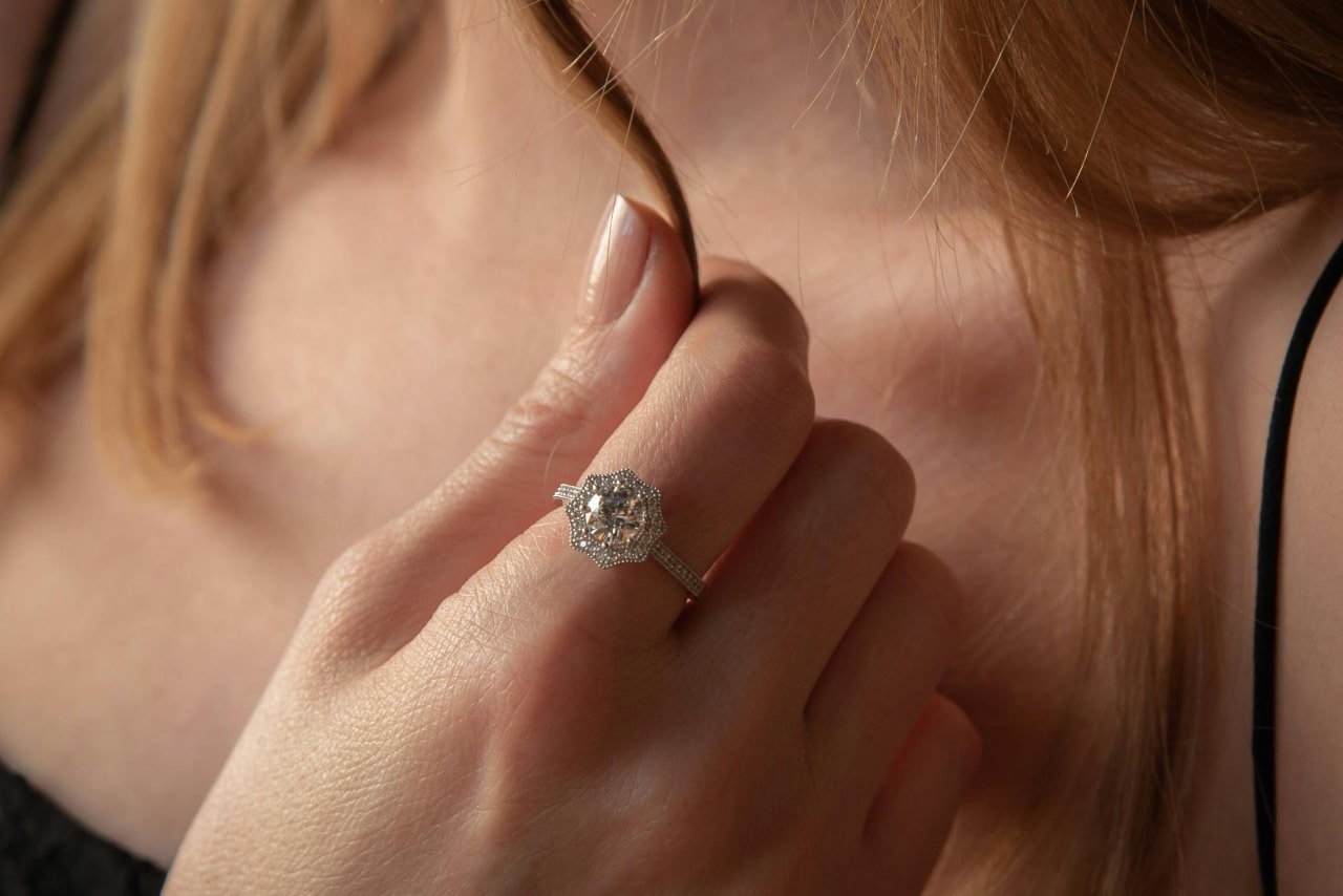 A blooming halo around a platinum diamond ring with a round center stone and diamonds along the band on a woman’s hand holding a strand of her hair