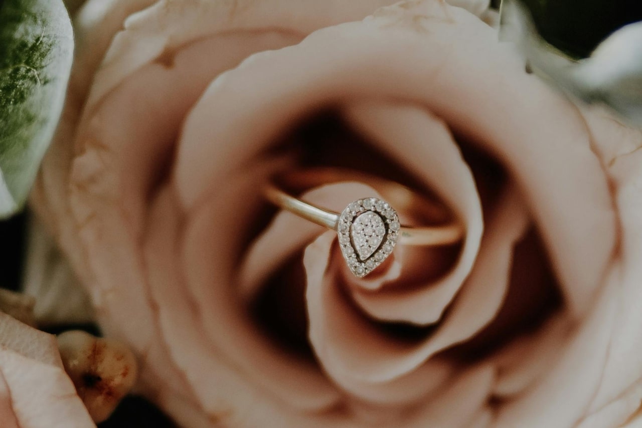 Pear shaped diamond with a halo of round diamonds for this halo ring with a yellow gold band sitting in the middle of a blush rosh
