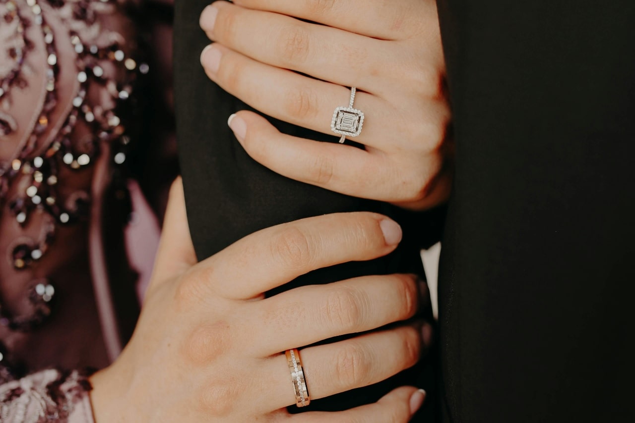 A woman holding onto her groom’s arm with a display on her halo engagement ring and band on her other hand.