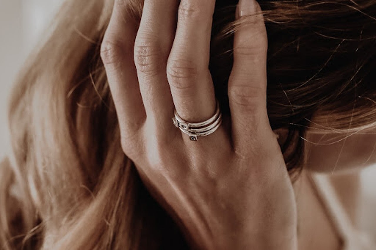 A woman running her hand through her golden hair and showcasing 3 silver rings stacked on her ring finger.