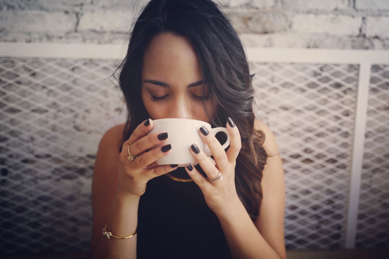 A woman with black nails and gold jewelry, bracelet, necklace, rings, drinking out of a coffee cup A woman with black nails and gold jewelry, bracelet, necklace, rings, drinking out of a coffee cup