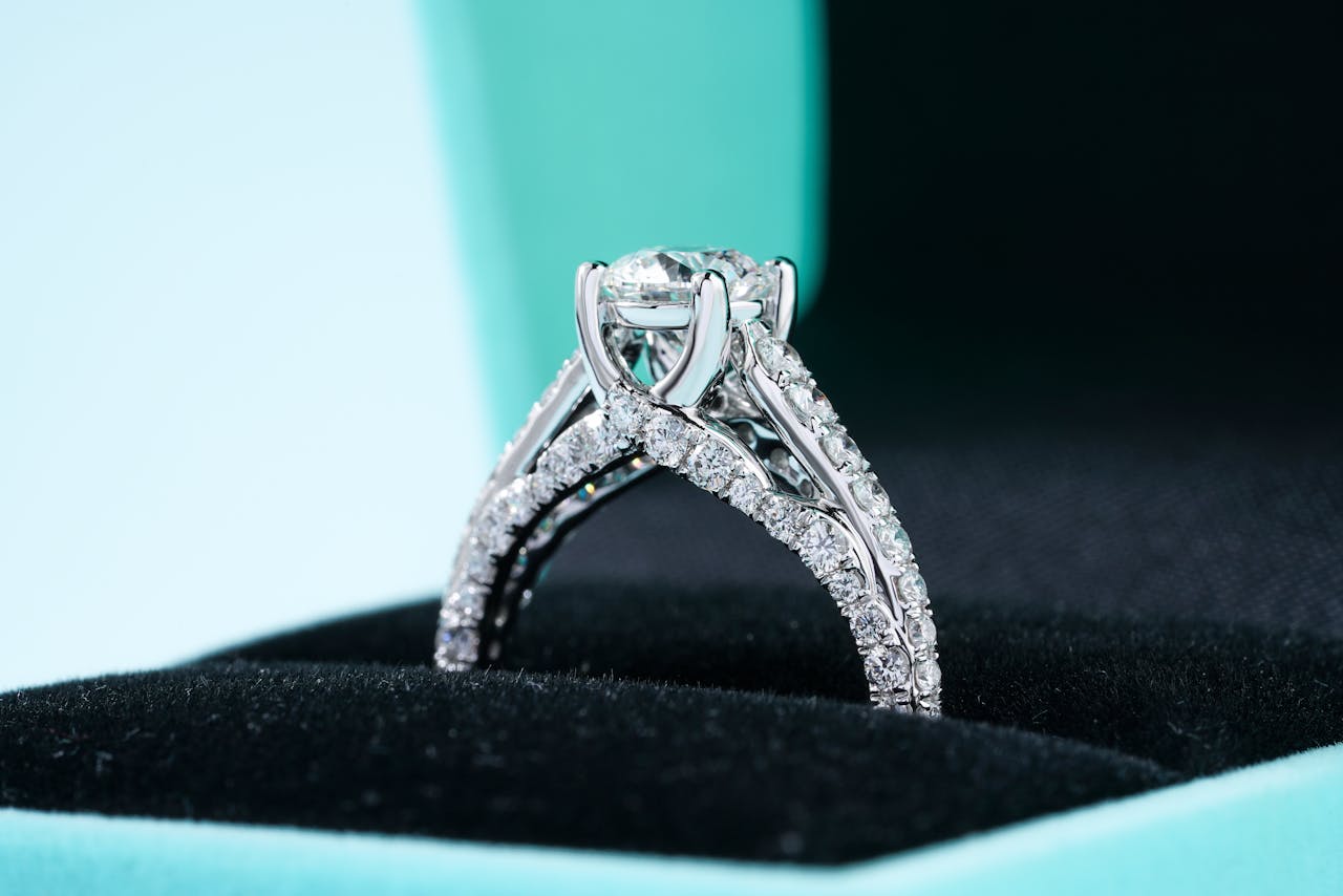 A close-up of an ornate cathedral-style side stone engagement ring displayed in its box.