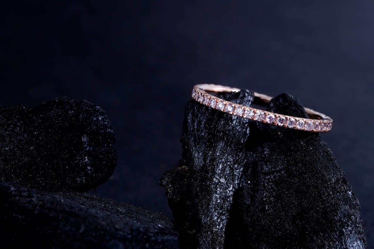 A delicate rose gold side stone engagement ring displayed atop dark stone.